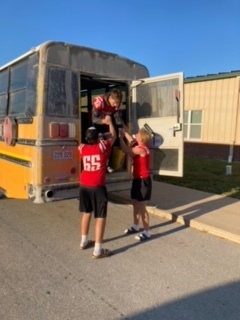 Image of two students assisting a third out of the emergency exit of a school bus.